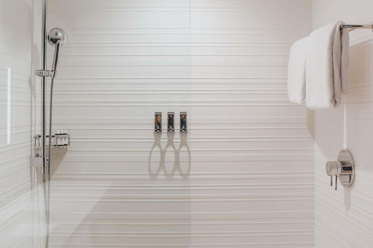 A modern bathroom with a glass shower enclosure, a handheld showerhead, a wall-mounted faucet, and a towel rack.