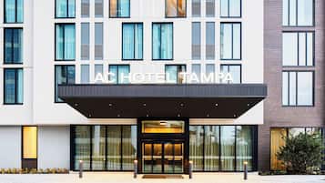 A modern hotel entrance with a glass facade, a covered entrance area, and the name "AC HOTEL TAMPA" displayed above the doors.