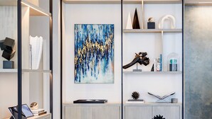 A modern living room with a white sofa, a coffee table with a vase of green plants, and a bookshelf with various decorative items and a painting. - AC Hotel by Marriott Tampa Airport (Tampa)