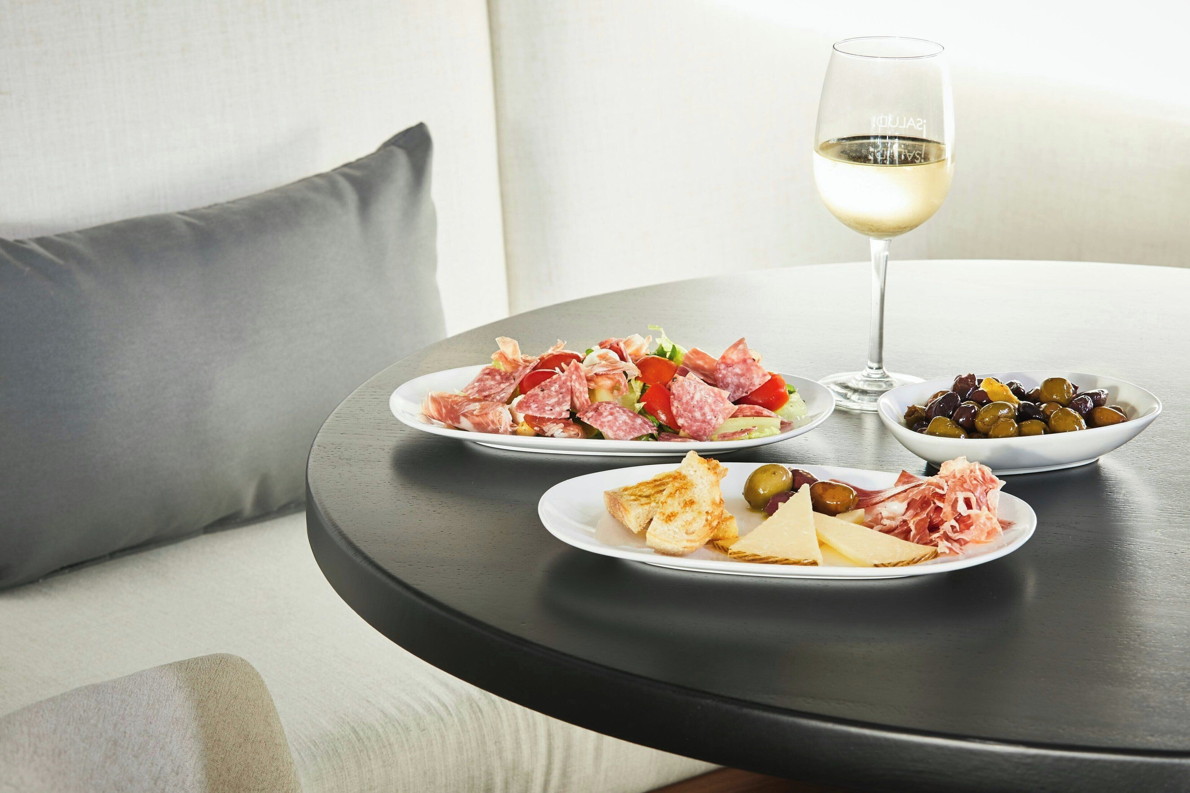 Une table ronde avec des assiettes de nourriture et un verre de vin blanc.
