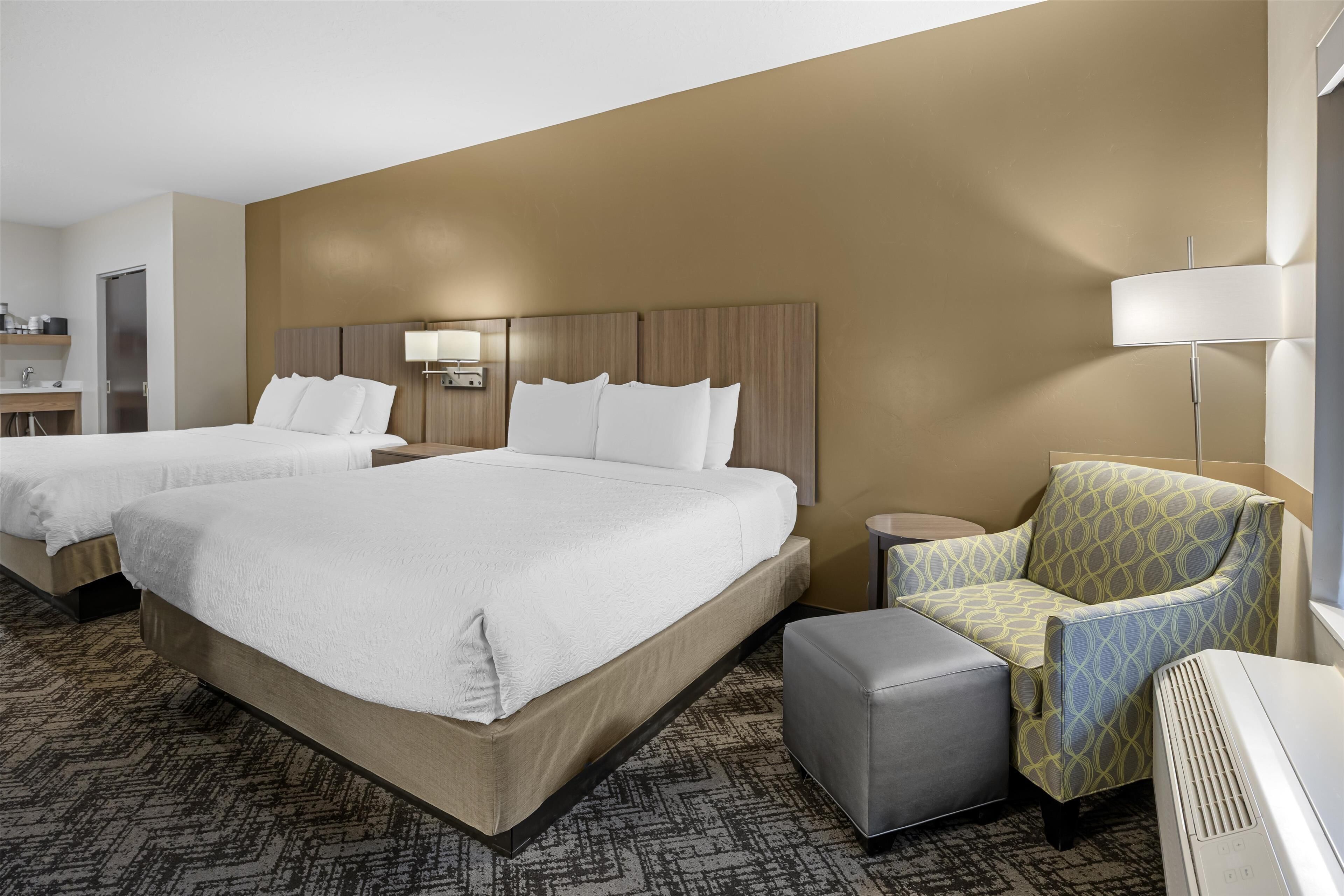 A hotel room with two beds, a desk, a chair, and a lamp.