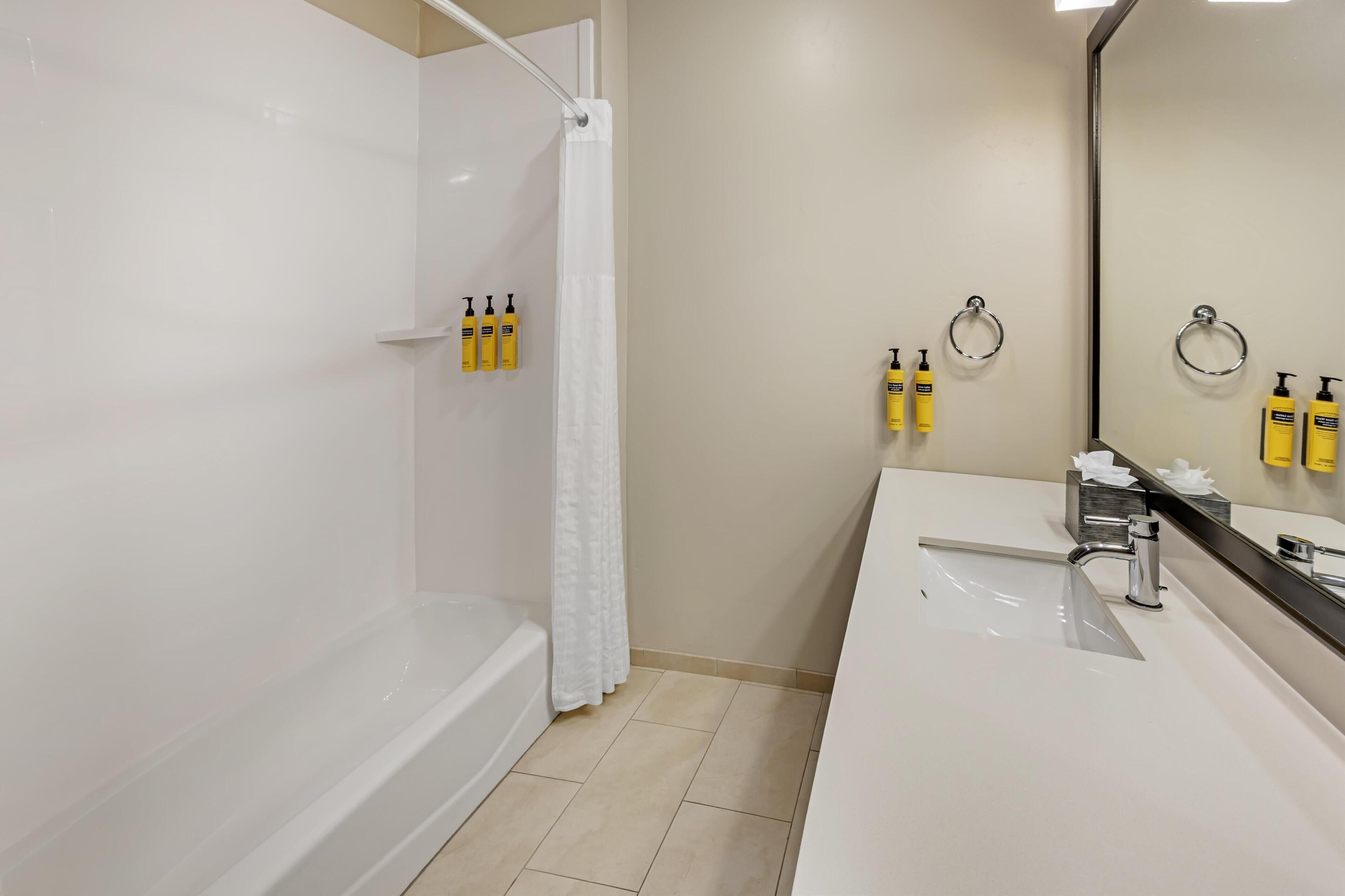 A modern bathroom with a bathtub, a shower with a curtain, and a vanity with a mirror and toiletries.