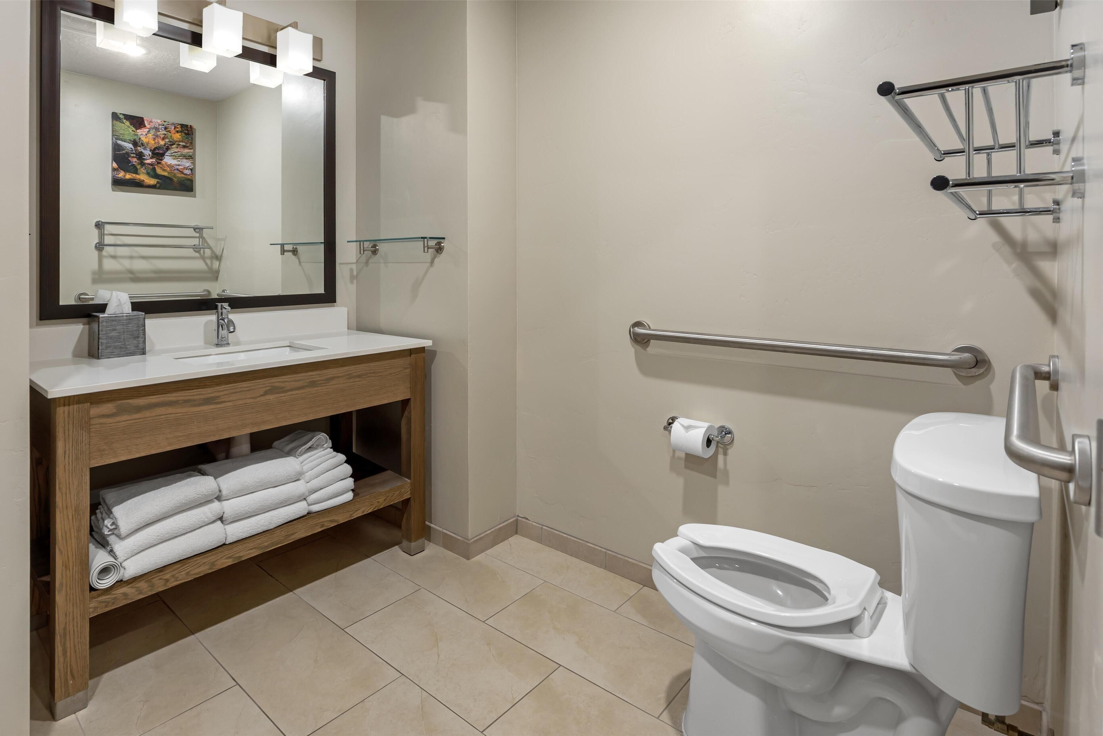 A bathroom with a wooden vanity, a large mirror, a toilet, and a glass shelf.