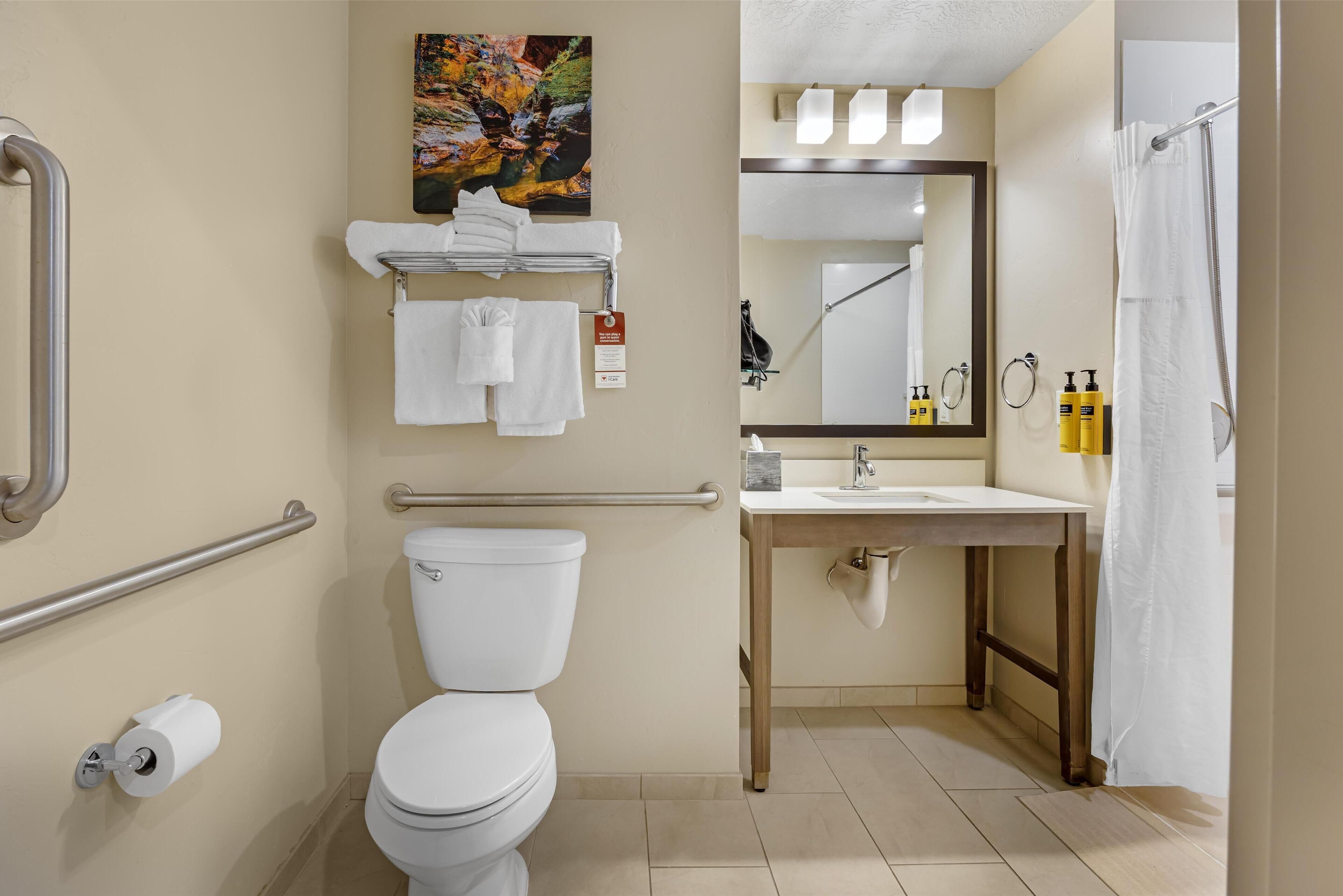 Un baño con inodoro, barras de apoyo, lavamanos y cortina de ducha.