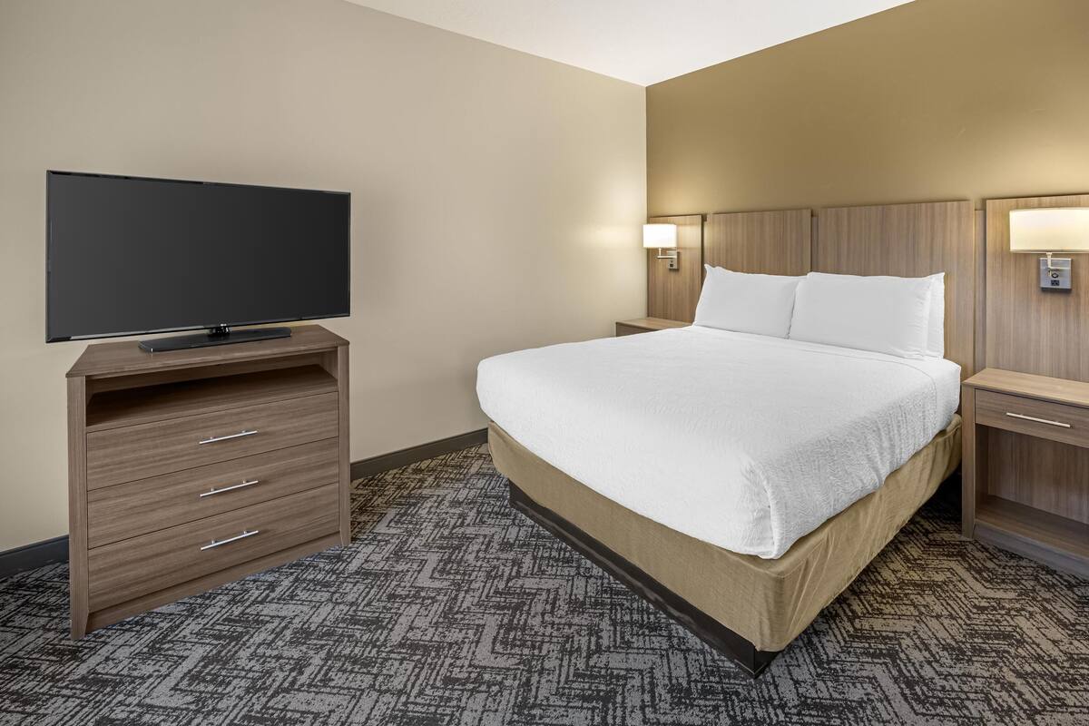 A hotel room with a large bed, a flat-screen TV on a wooden dresser, and two bedside lamps.