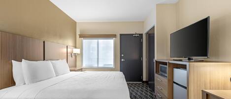 A hotel room with a large bed, a flat-screen TV, a minibar, and a door to a bathroom.