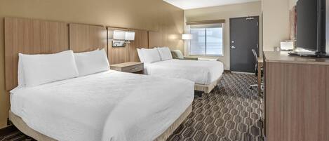 A hotel room with two beds, a desk, a TV, and a door.