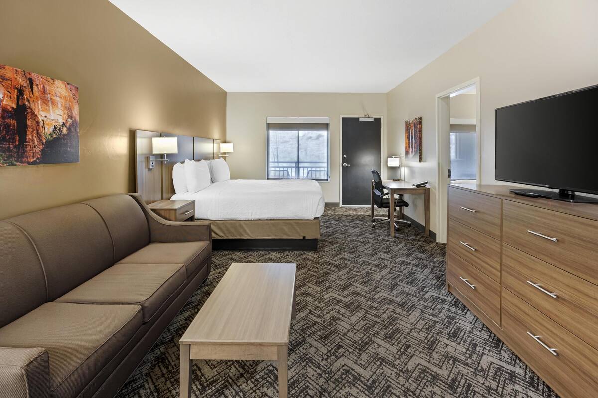 A hotel room with a bed, a sofa, a desk, a television, and a large painting on the wall.