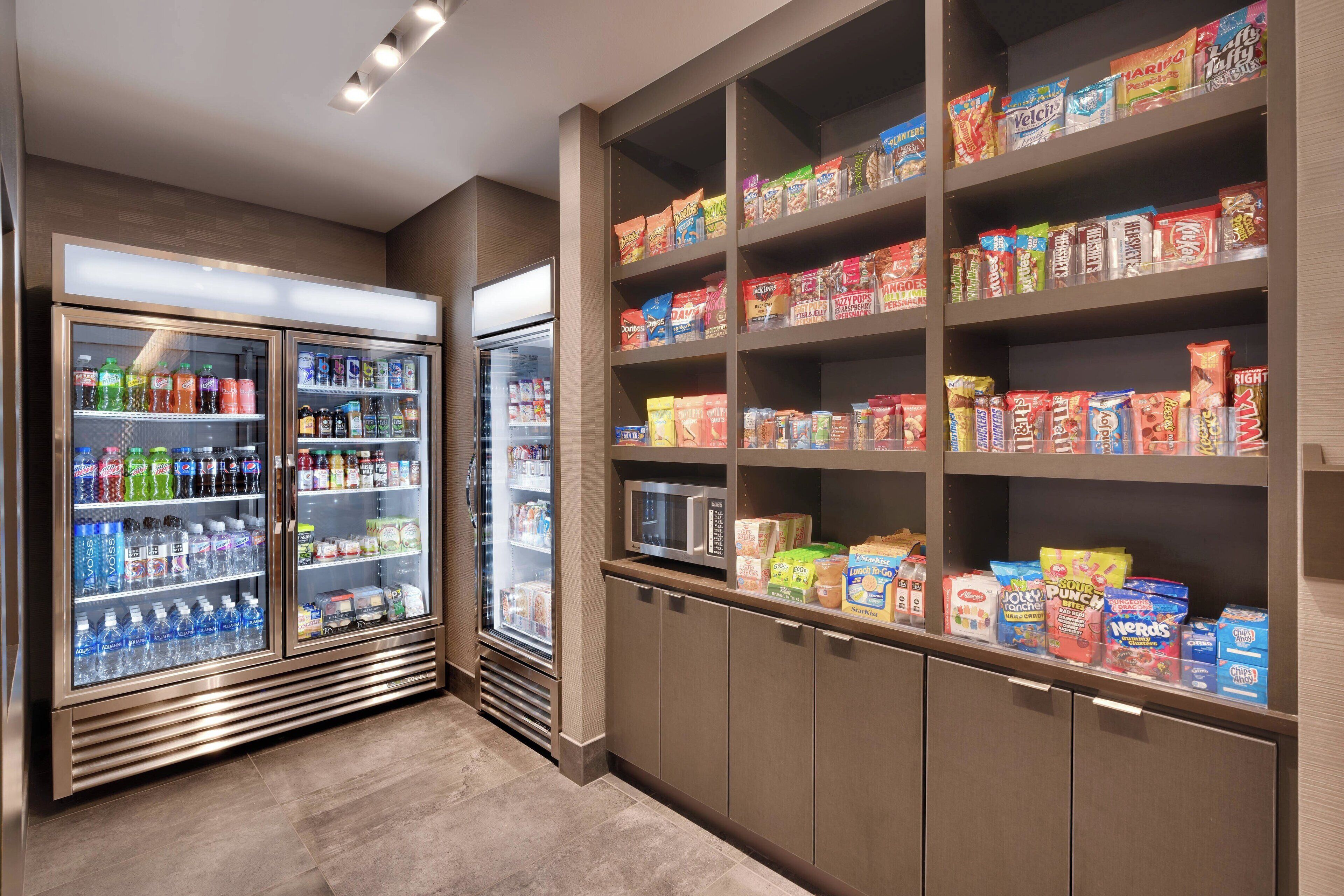 A self-service snack and beverage area with refrigerated drinks and shelves stocked with various snacks and cereals.