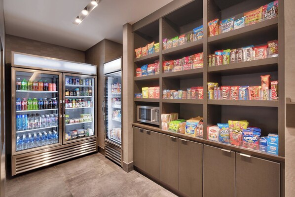 Un espacio autoservicio con bebidas refrigeradas y estantes llenos de diferentes aperitivos y cereales.