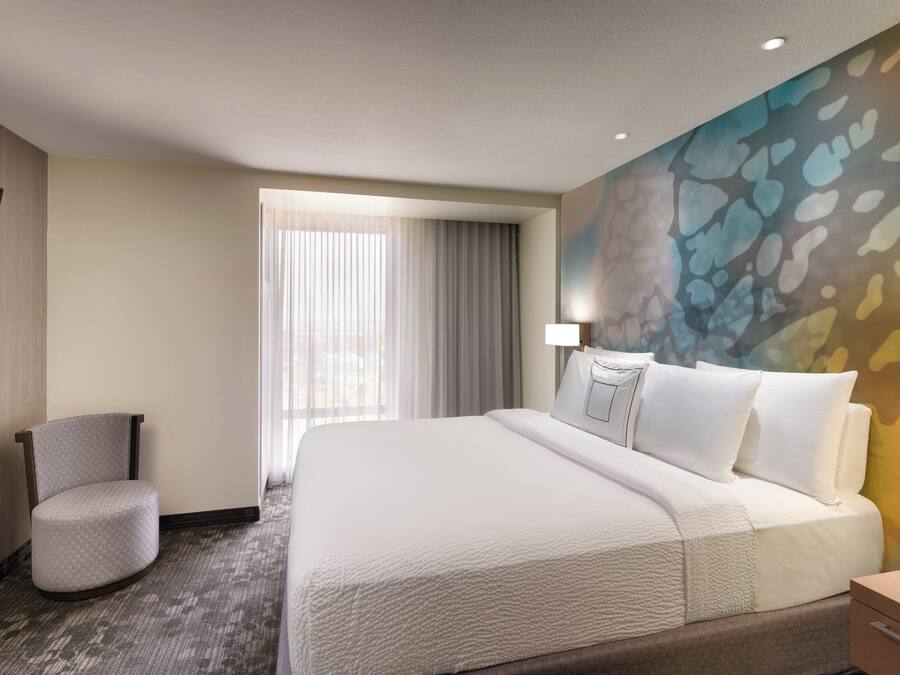 A hotel room with a large bed, a chair, a desk, and a painting on the wall.