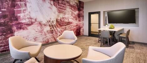 A modern meeting room with a large abstract mural, comfortable seating, a round table, and a flat-screen TV.