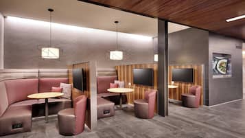 A modern interior with a seating area featuring cushioned sofas and round tables, a wooden ceiling, and a flat-screen TV on the wall.