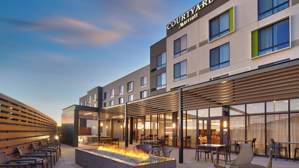 Exterior de um hotel Courtyard Marriott, com área de estar ao ar livre, lareira e um terraço coberto.