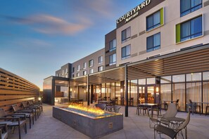 Exterior de un hotel Courtyard Marriott, con mobiliario exterior, una chimenea y un porche cubierto.
