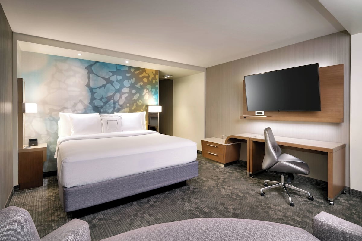 Une chambre d’hôtel dotée d’un grand lit, d’un bureau, d’une chaise, d’un téléviseur à écran plat et d’un mur orné d’un motif abstrait aux couleurs vives.