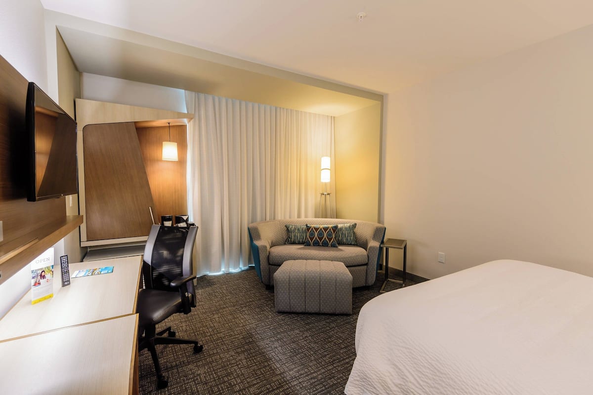 Ein Hotelzimmer mit einem Bett, einem Schreibtisch mit Computer, einem Sessel und einer Couch sowie einem Fernseher.