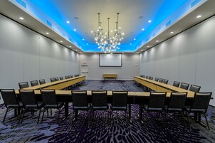 Un salón de conferencias con una larga mesa, sillas, una pantalla de proyector y un candelabro.