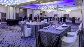 Een feestzaal met ronde tafels gedekt voor het diner, een podium en een grote kroonluchter.