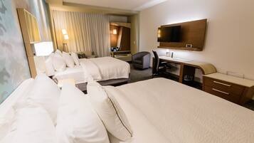 A hotel room with two beds, a desk, a chair, a TV, and a bathroom with a shower and toilet.