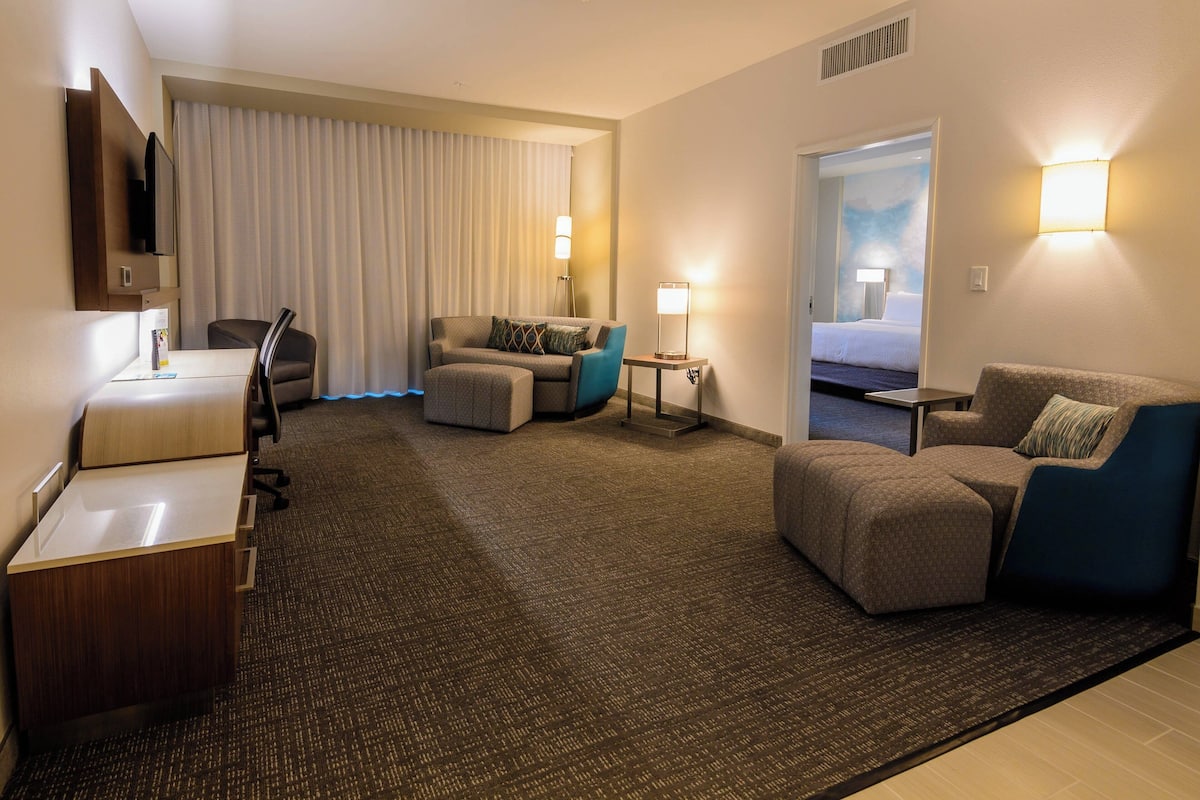 Ein Hotelzimmer mit Schreibtisch, einer Couch, einem Sessel, einem kleinen Tisch, einer Lampe und einem Bett.