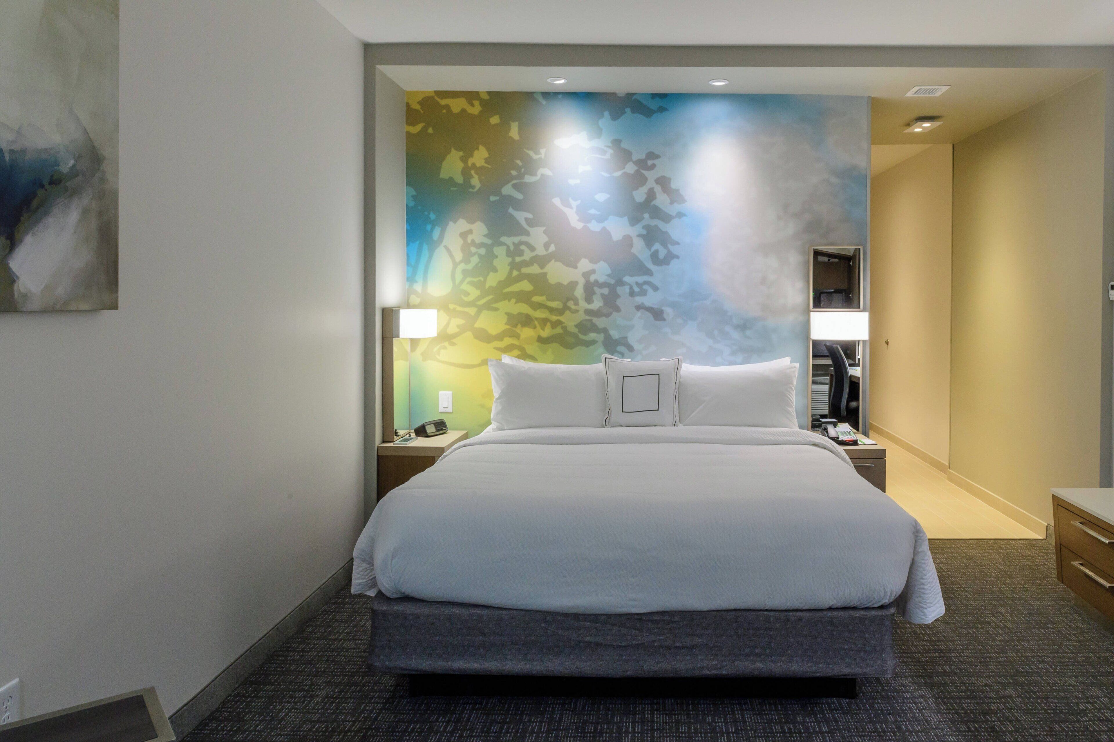 A hotel room with a large bed, a nightstand, a lamp, and a wall with a camouflage pattern.
