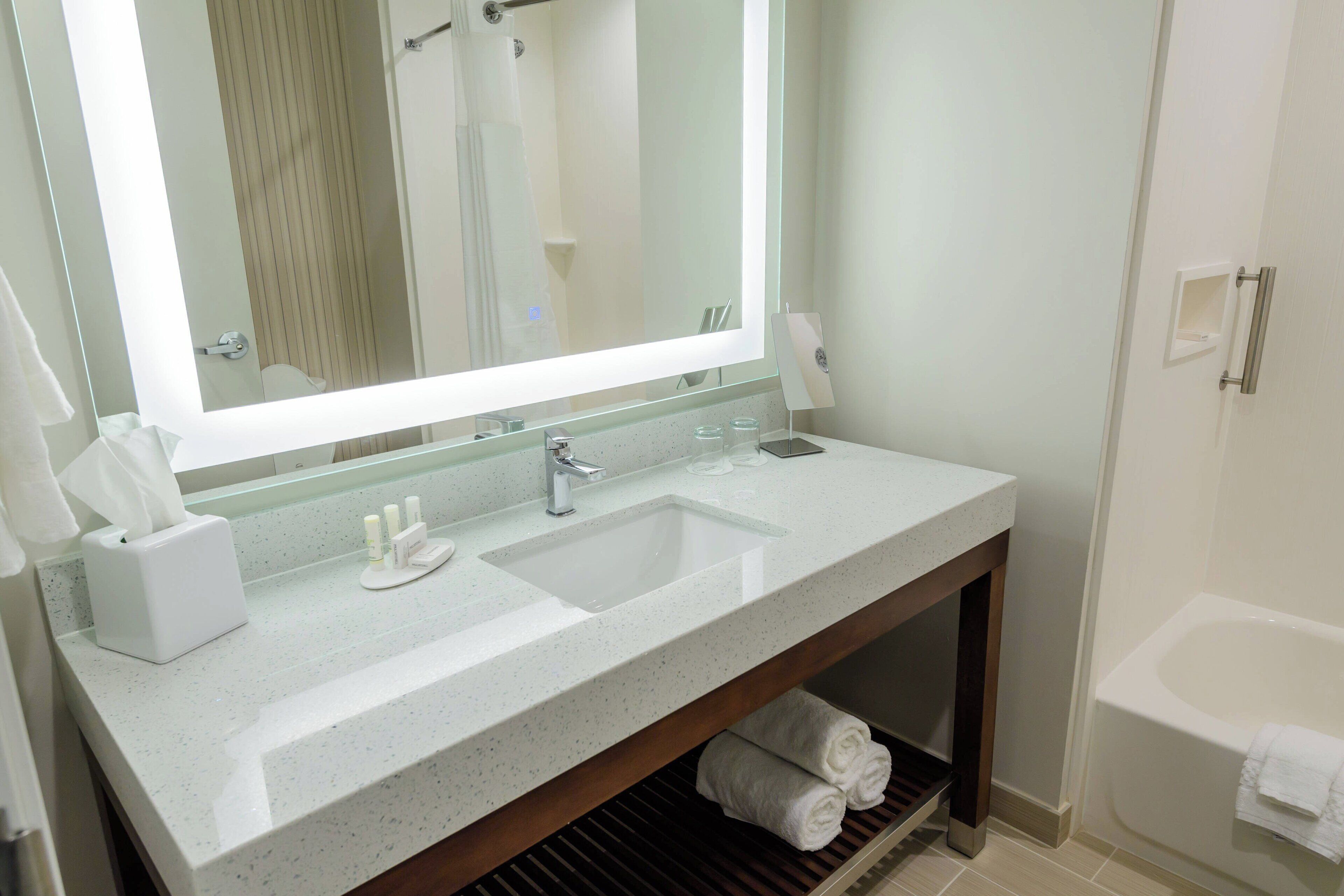 A bathroom with a large mirror, a sink, a vanity, and a bathtub.