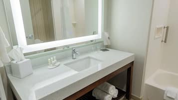 A bathroom with a large mirror, a sink, a vanity, and a bathtub.