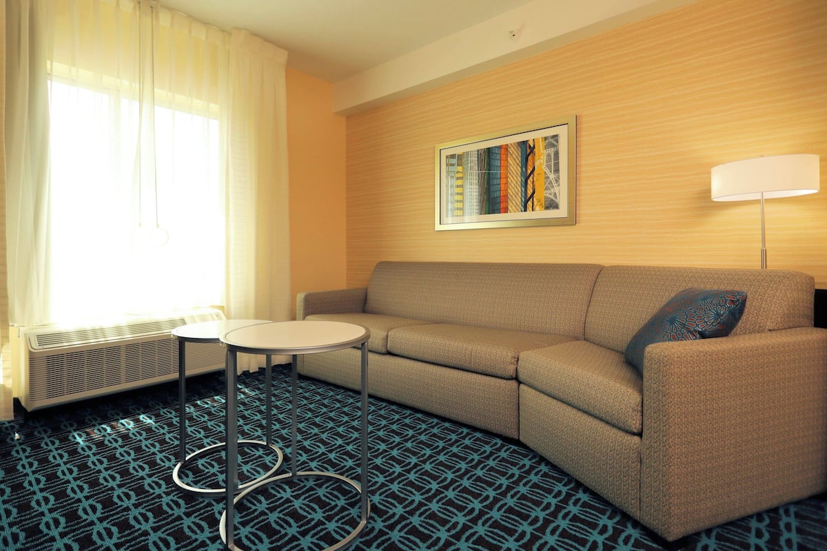 A hotel room with a sofa, a small round table, a radiator, and a framed picture on the wall.
