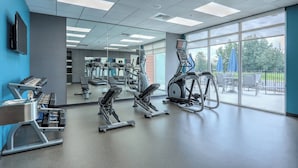 Un gimnasio con máquinas de cardio, bancos de pesas y un amplio ventanal con vistas al exterior.