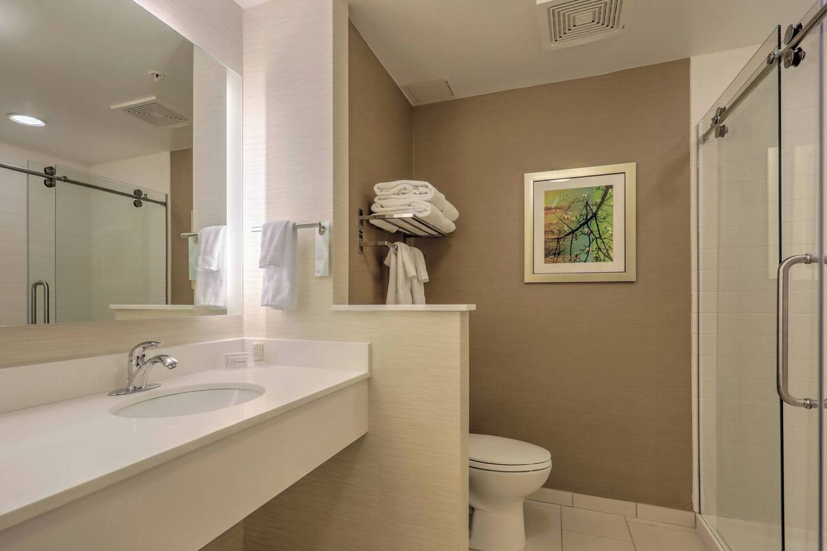 A modern bathroom with a large mirror, a sink, a toilet, and a glass shower enclosure.