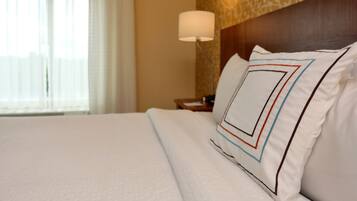 A neatly made bed with white linens and a pillow featuring a geometric pattern.