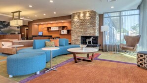 Un vestíbulo de hotel moderno con chimenea de piedra, un mostrador de recepción y una zona de estar con sofá azul y mesas redondas.