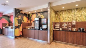 Zona de recepción de hotel con mostrador de madera, una máquina de café y una exhibición de frutas.
