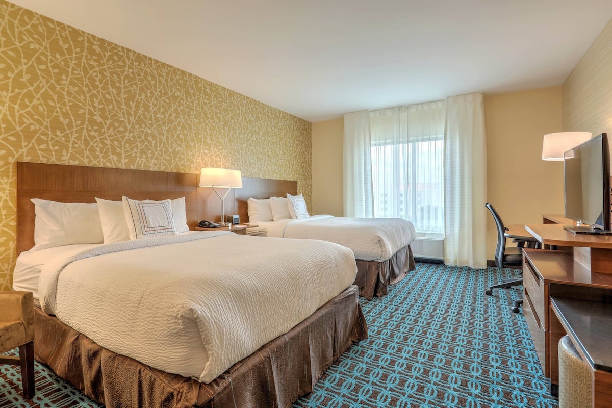 A hotel room with two beds, a desk, a chair, a TV, and a window with curtains.