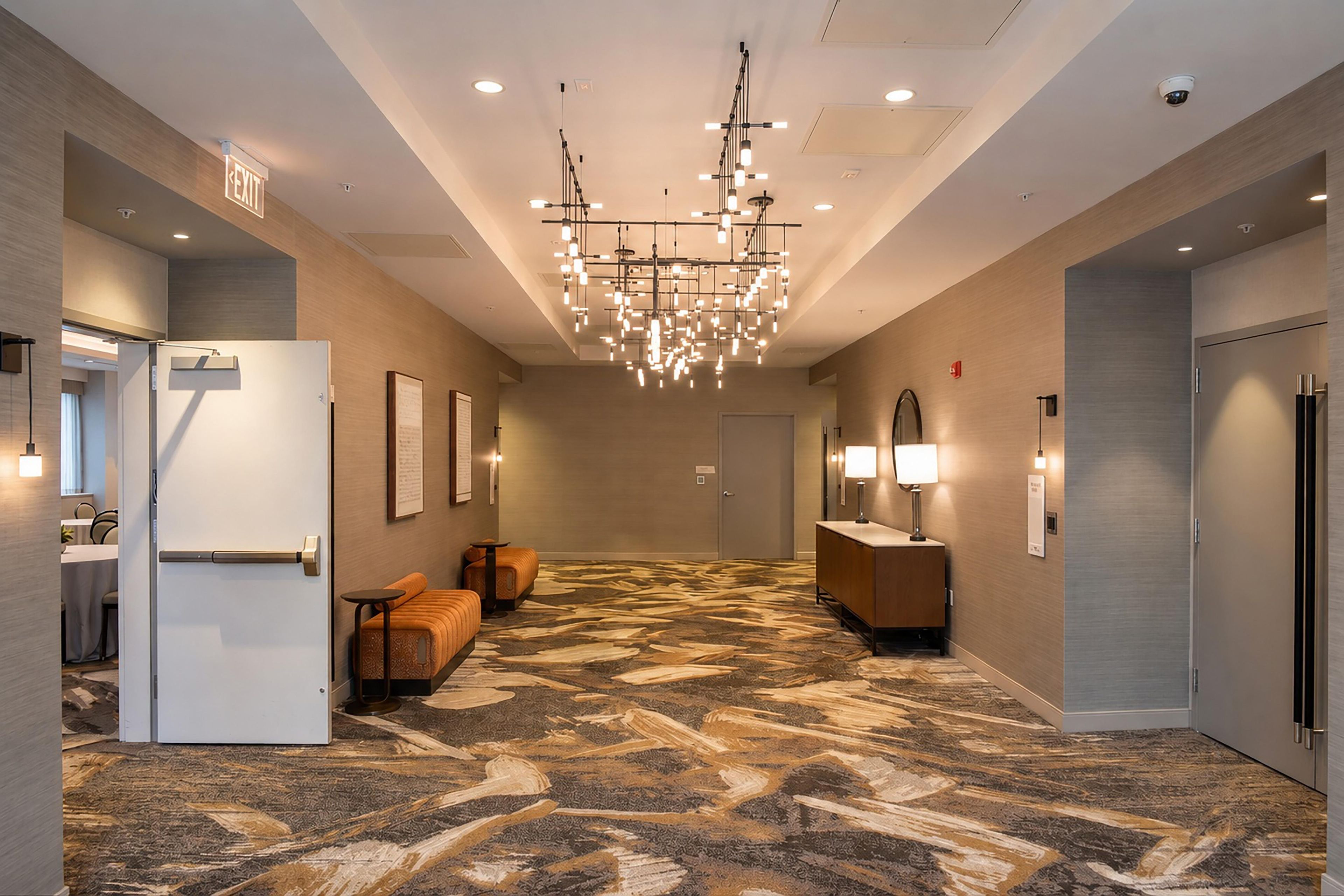 Un hall de hotel con alfombra estampada, una araña y mostradores de recepción, además de zonas de estar.