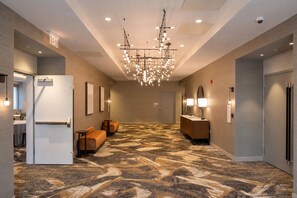 Un hall de hotel con alfombra estampada, una araña y mostradores de recepción, además de zonas de estar.