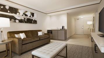 A modern hotel room with a sofa, a coffee machine, a TV, and a small kitchenette.