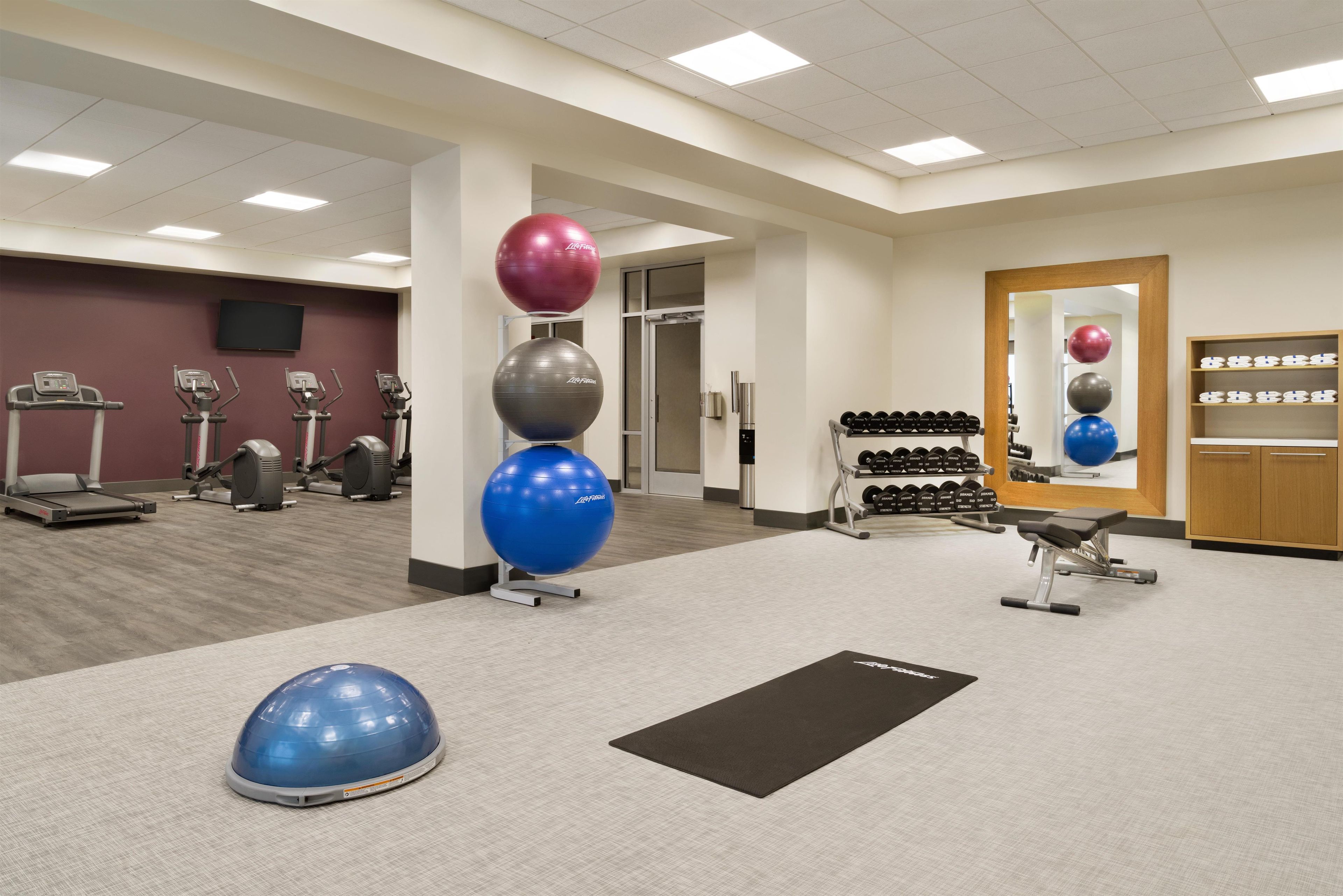 A gym with exercise equipment, a mirror, and a wall-mounted television.