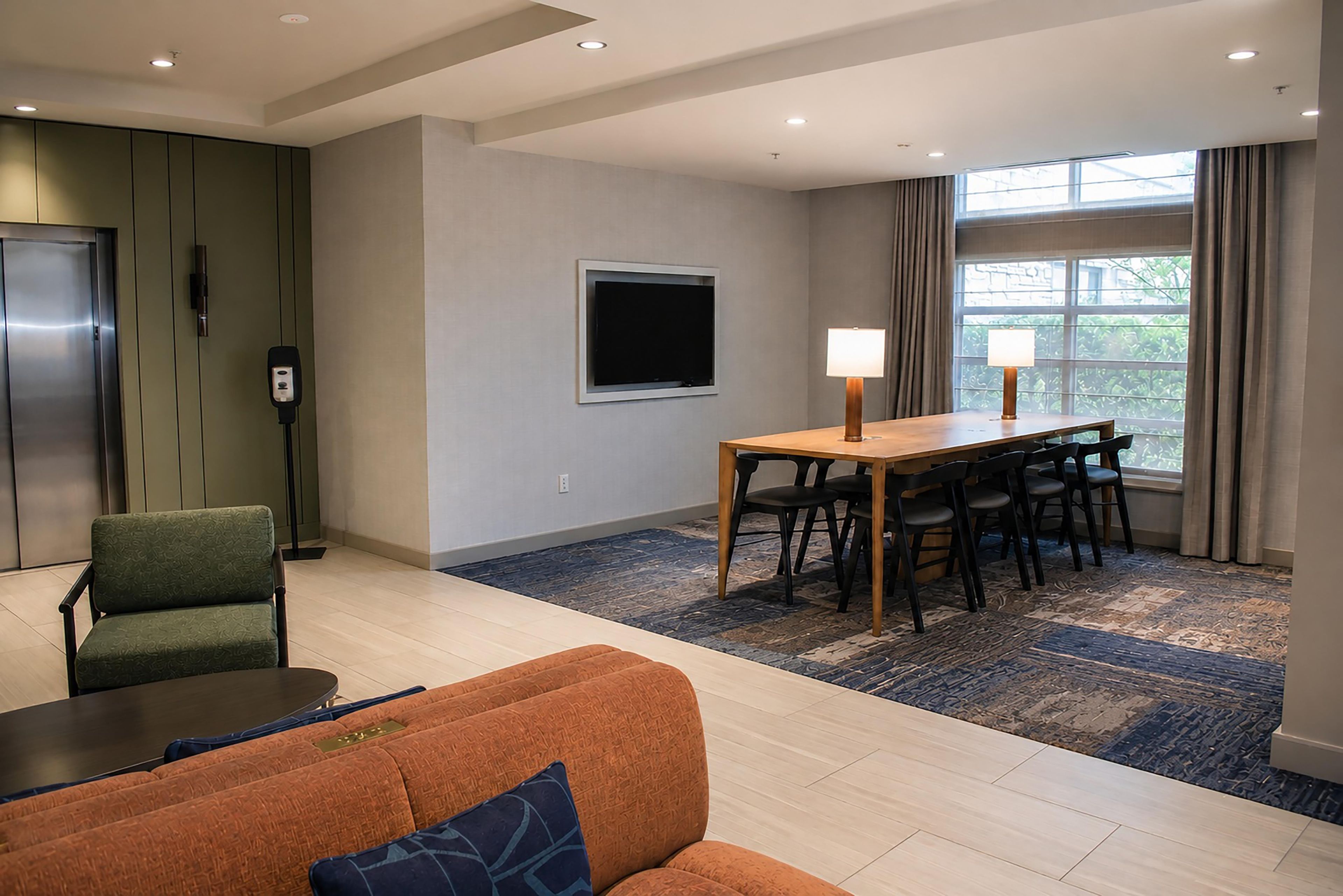 A hotel room with a dining area, a sofa, a TV, and a window with curtains.