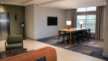 A hotel room with a dining area, a sofa, a TV, and a window with curtains.