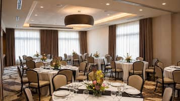 Une salle de banquet avec des tables rondes, des chaises et un lustre central.