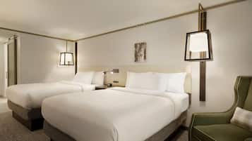 A hotel room with two beds, a nightstand, a lamp, a painting, and a green armchair.