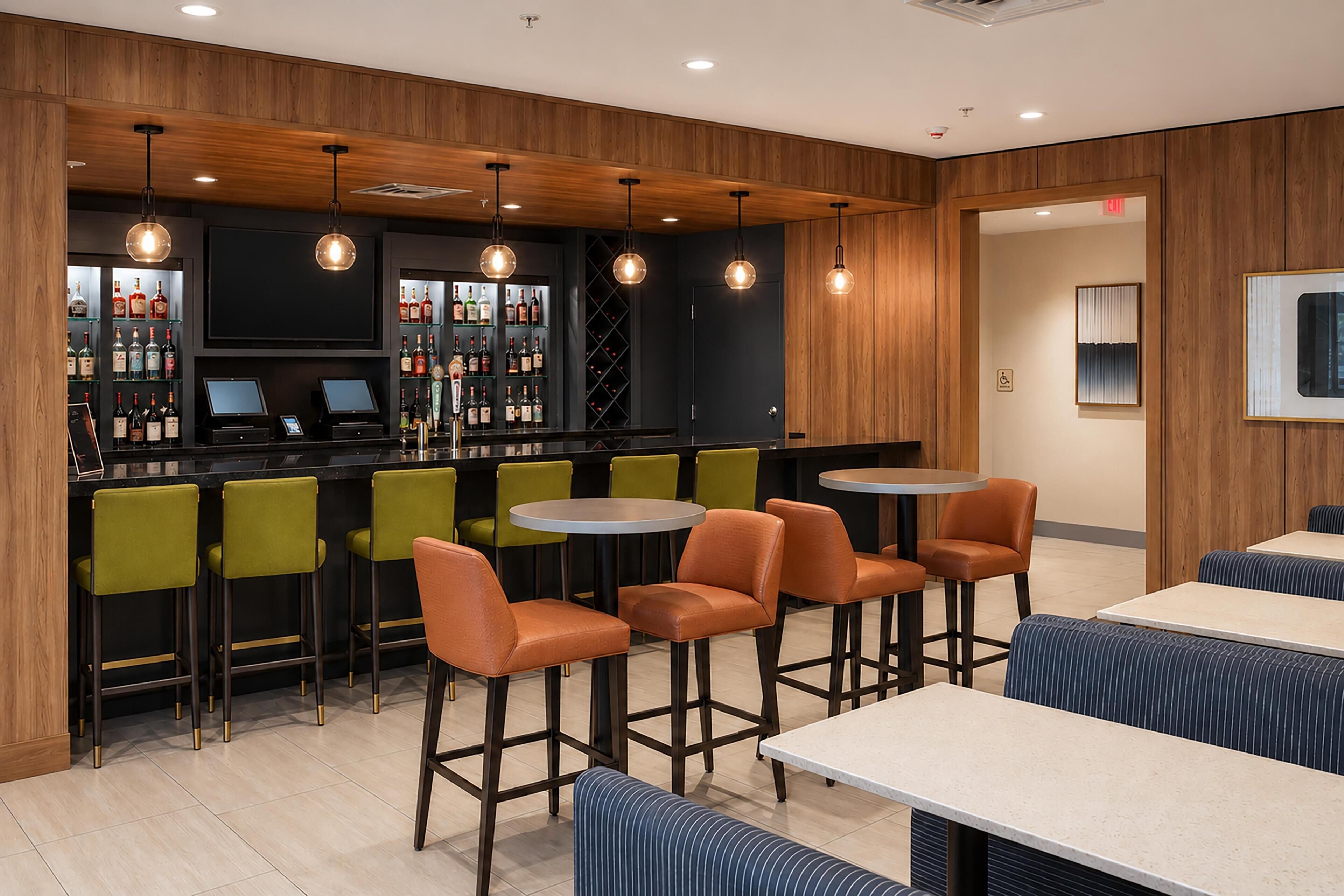 A bar area with multiple stools, a counter with a cash register, and a wine rack.