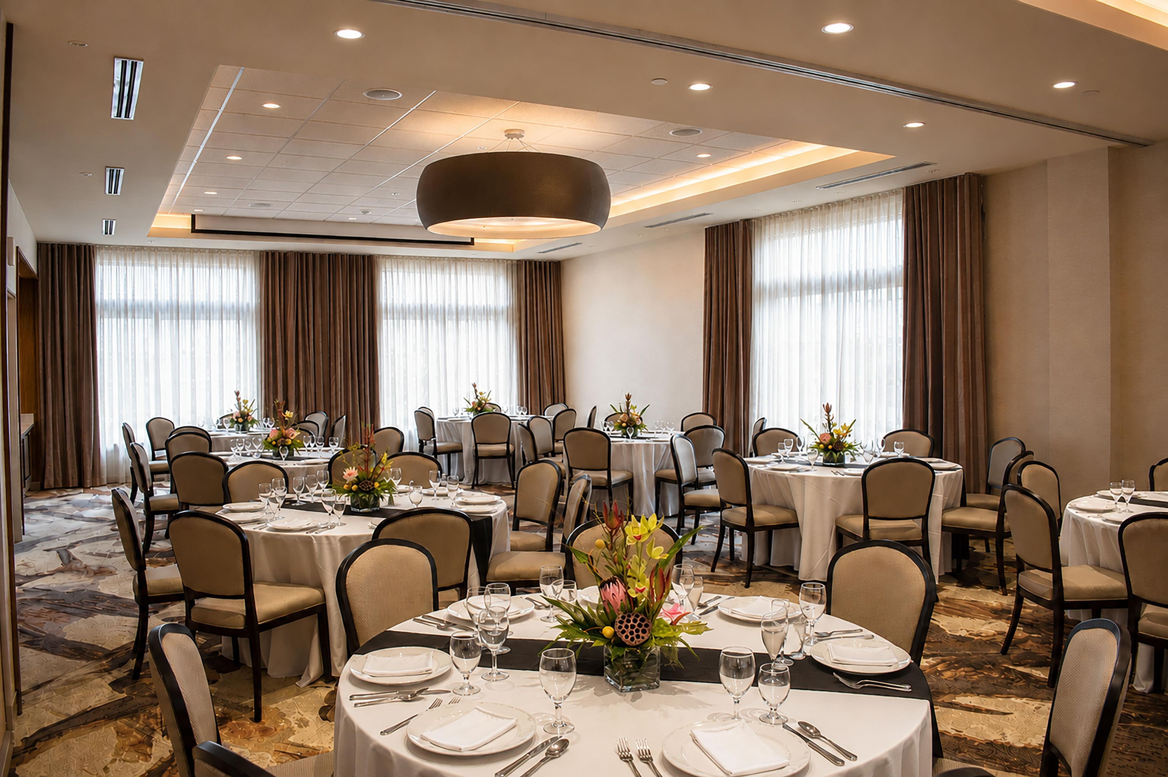A banquet hall with round tables, chairs, and a central chandelier.