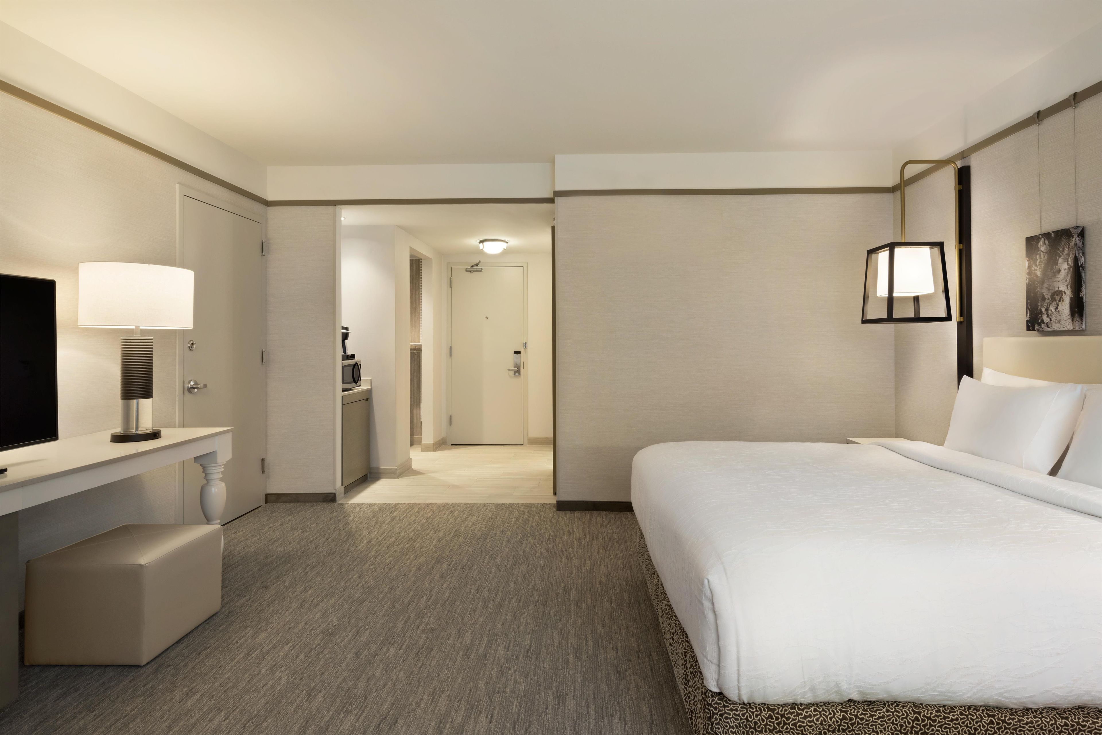 Habitación de hotel con cama, escritorio con lámpara, televisión y baño visible a través de una puerta abierta.
