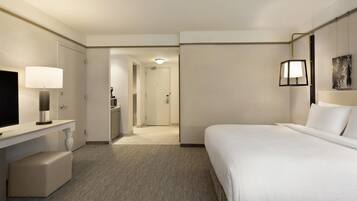 Habitación de hotel con cama, escritorio con lámpara, televisión y baño visible a través de una puerta abierta.