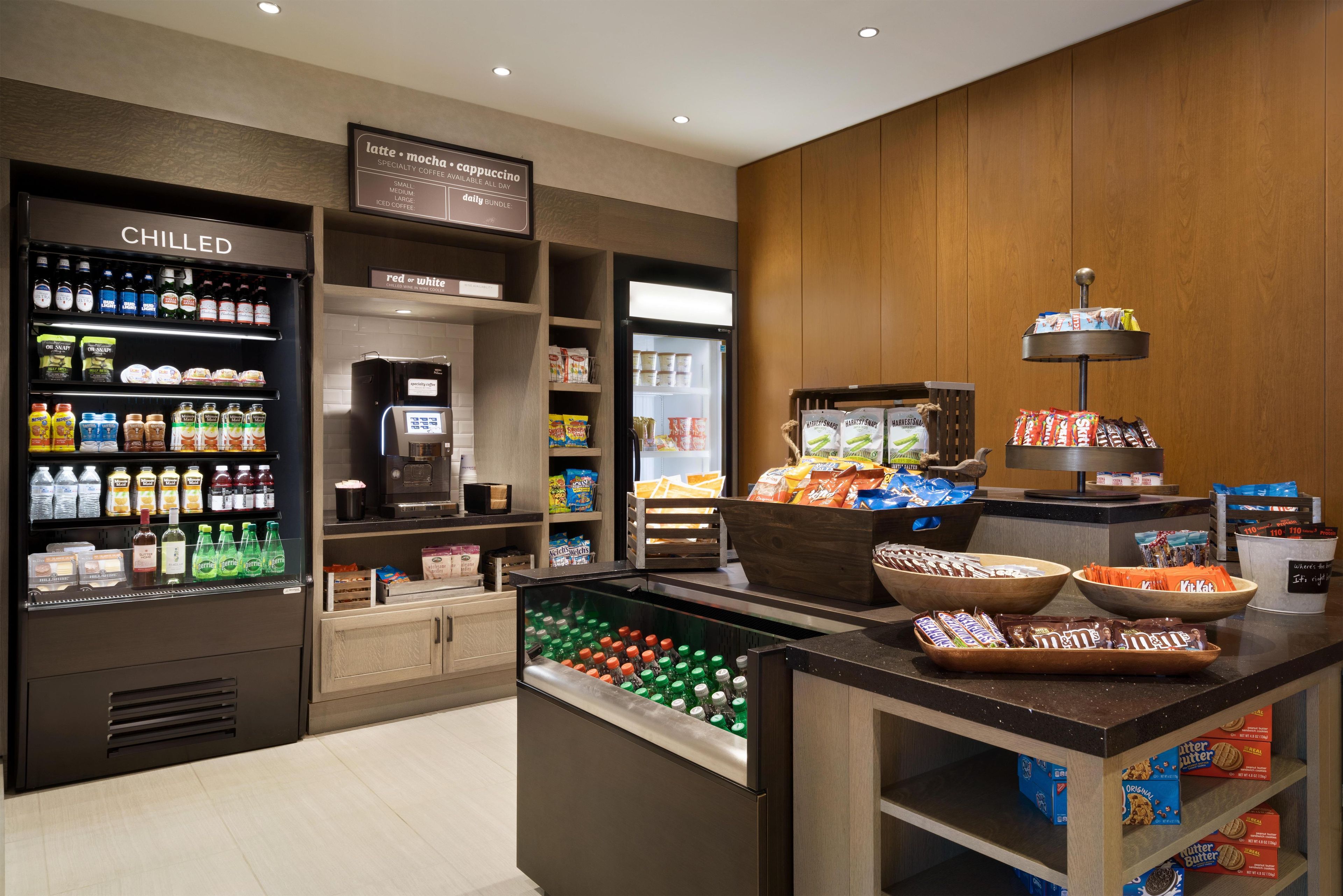 Una estación autoservicio con bebidas frías, una máquina de café y una variedad de bocadillos y galletas.