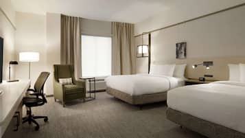 A hotel room with two beds, a desk, a chair, a lamp, and a painting on the wall.