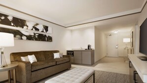 A modern hotel room with a sofa, a bench, a coffee machine, a TV, and a kitchen area. - Hilton Garden Inn Newtown Square Radnor (Newtown Square)